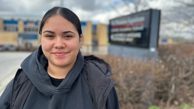 A young woman stands in front of a sign for St. Thomas Aquinas Catholic Secondary School in London Ontario