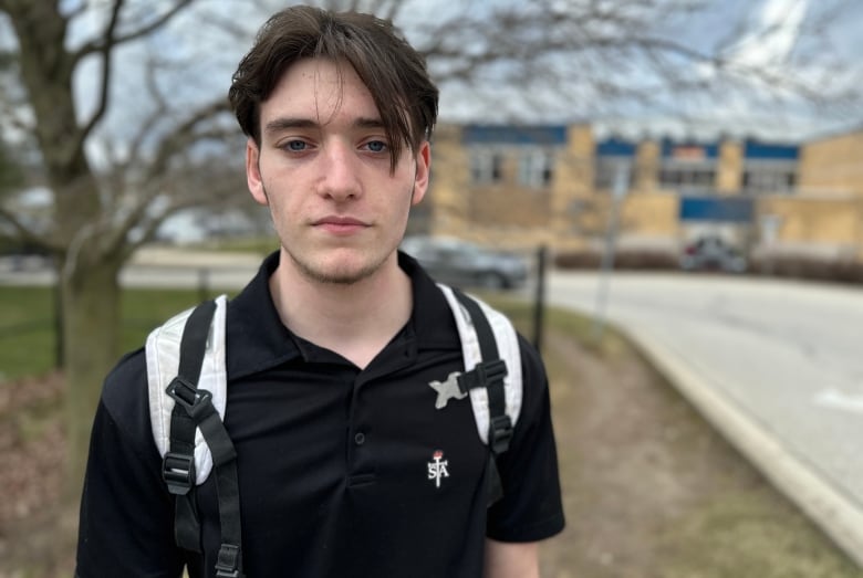 A young man stands outside. 