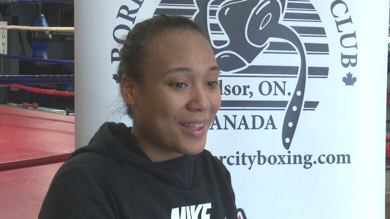 A female teen talks in front of a boxing ring.