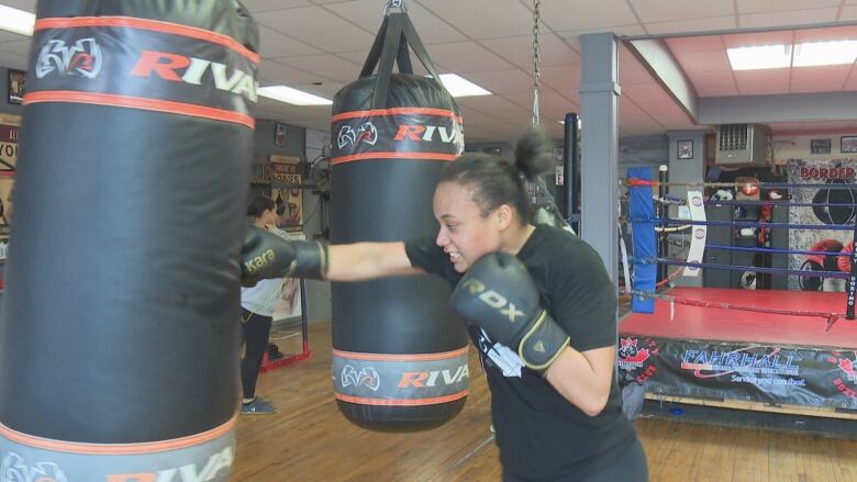 A teenage female boxer trains on a heavy bag.