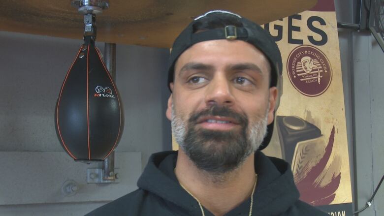 A male coach in a boxing club stands next to a speed bag.