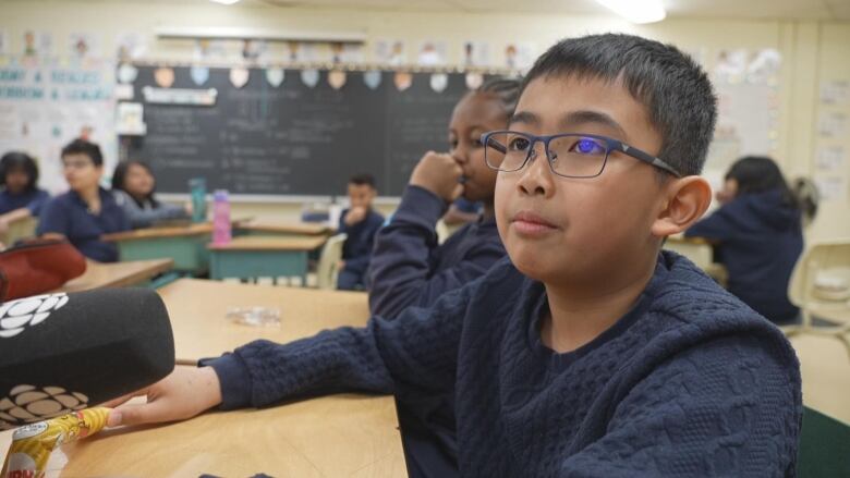 Screenshot from a classroom showing a boy in glasses speaking into a microphone.