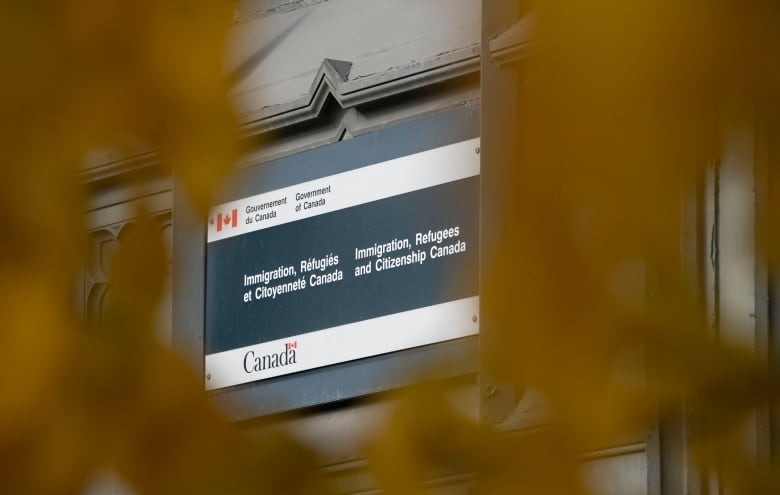 Foliage in foreground, office building with sign that read Immigration, Refugees and Citizenship Canada.