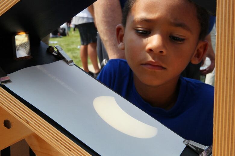 A young boy looks at a projected image of the solar eclipse as the moon starts to shield the sun during a partial solar eclipse.