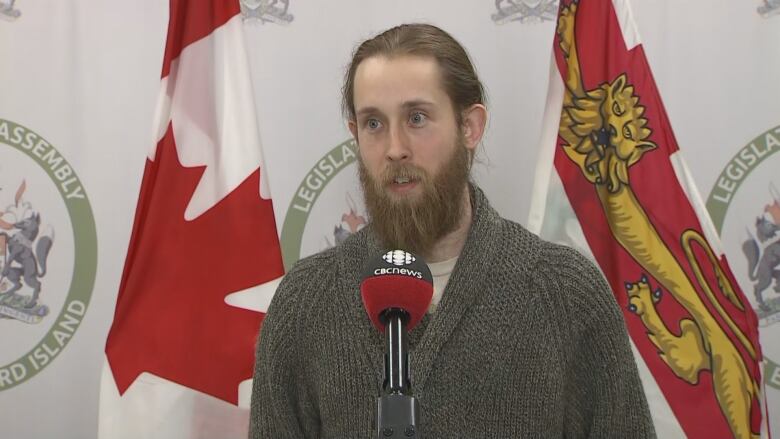 A bearded man with a green sweater in front of a PEI flag.