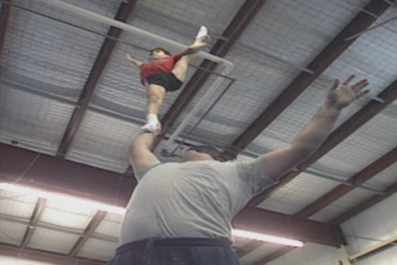 A large man balances a small boy on one hand , held high above his head.