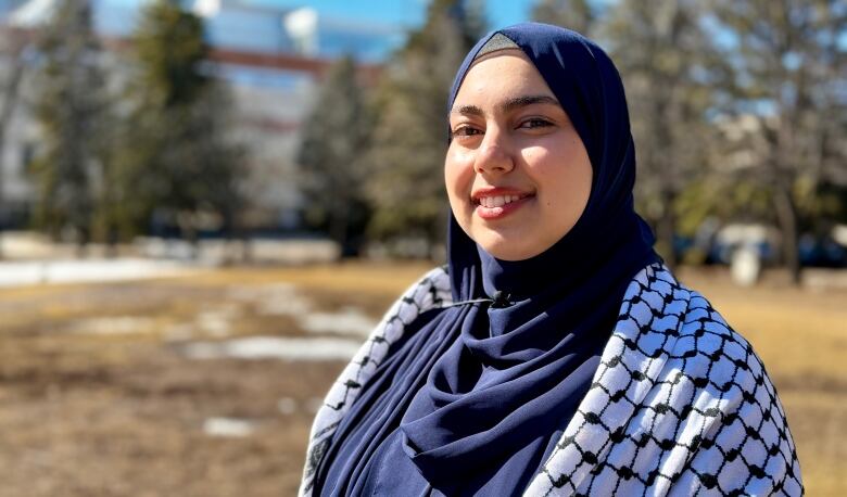 A woman wearing a headscarf and a Palestinian keffiyeh on her shoulders.