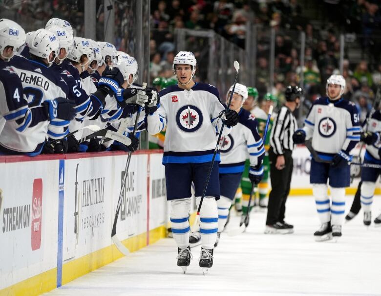 A hockey player skates alongside his team's bench. 