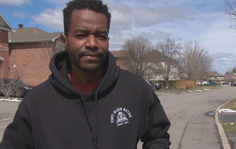 A Haitian man in a black hoodie stands in the street