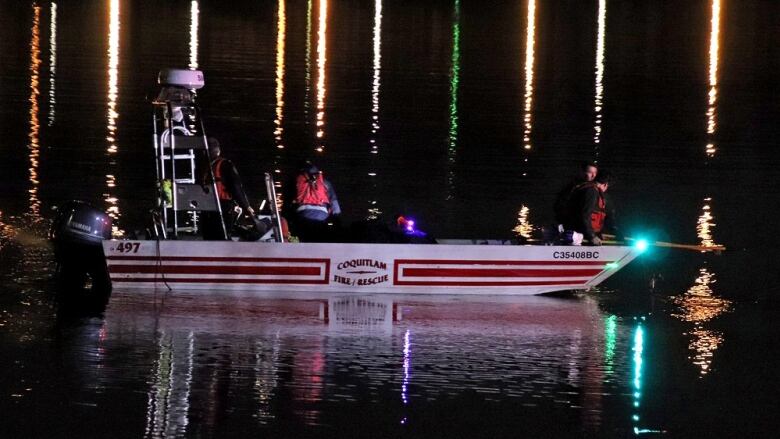 Firefighters in life vests on a boat look into the waters of a deep river at night.