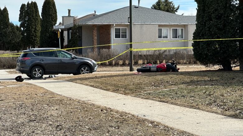 A car and a toppled motorcycle behind yellow tape.