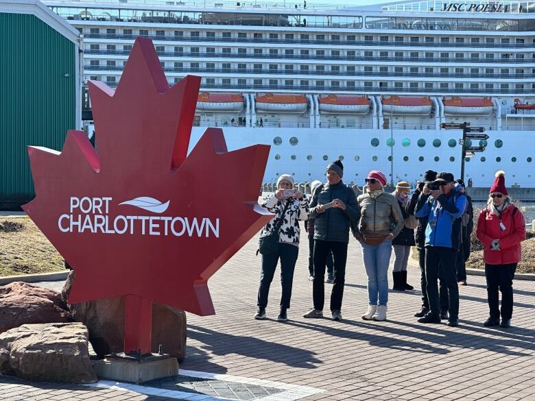 People taking photos of Port Charlottetown sign with cruise ship in background.