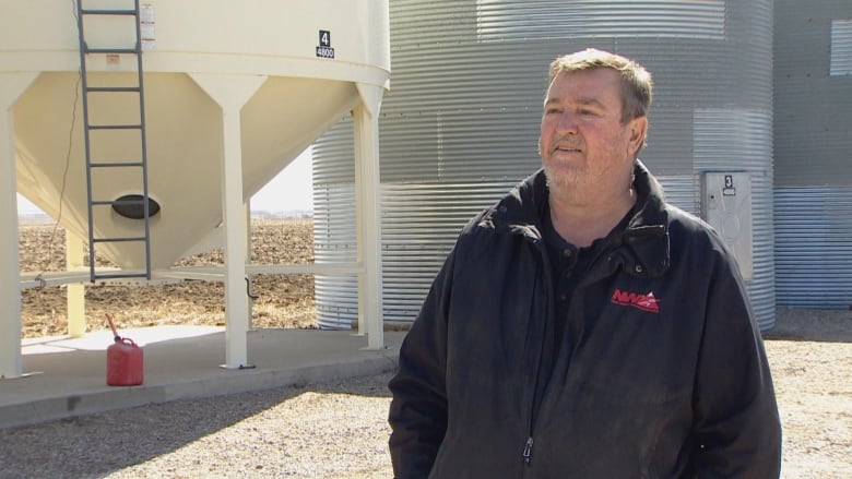 A man stands in front of grain bins.