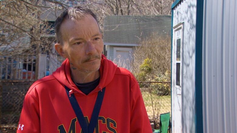 A man in a red sweater stands in front of a metal shelter