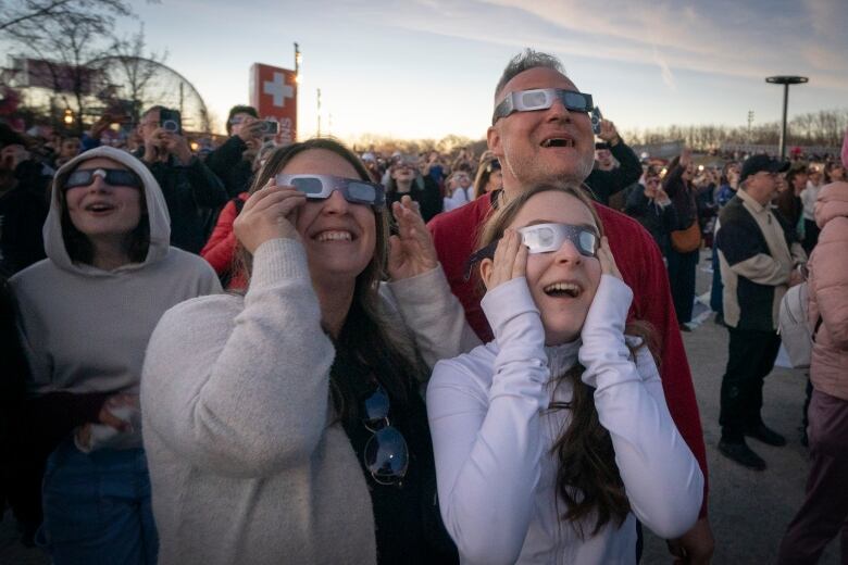 People smiling up at the sky wearing protective glasses.