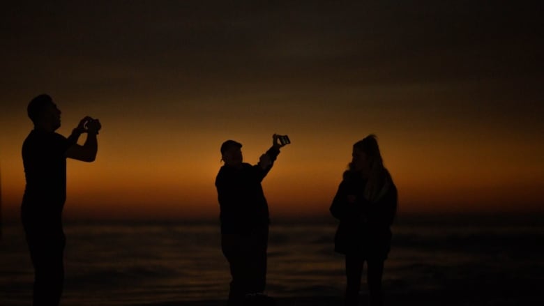 three people with phones in front of a red sunset