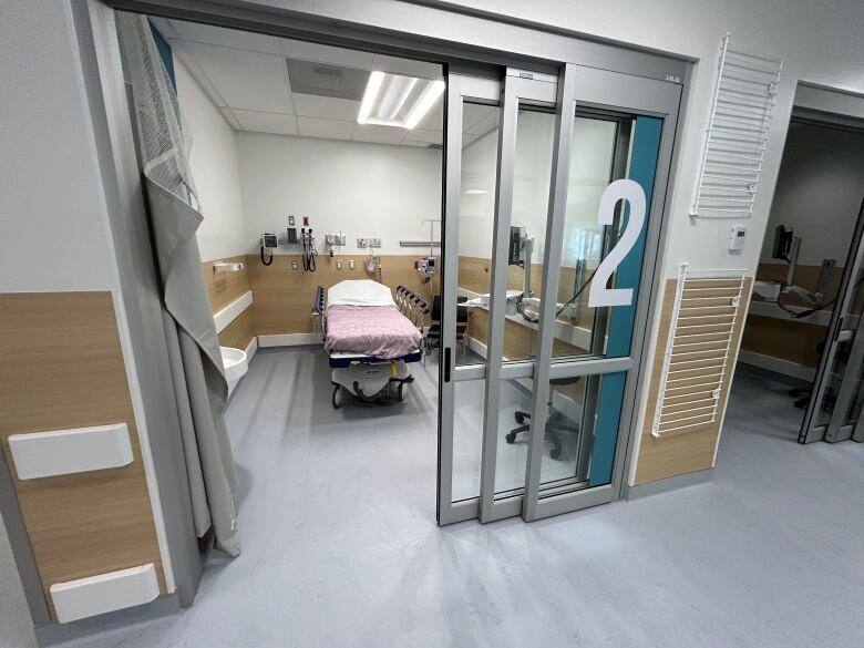 An empty hospital bed sits in a room behind a glass sliding door.