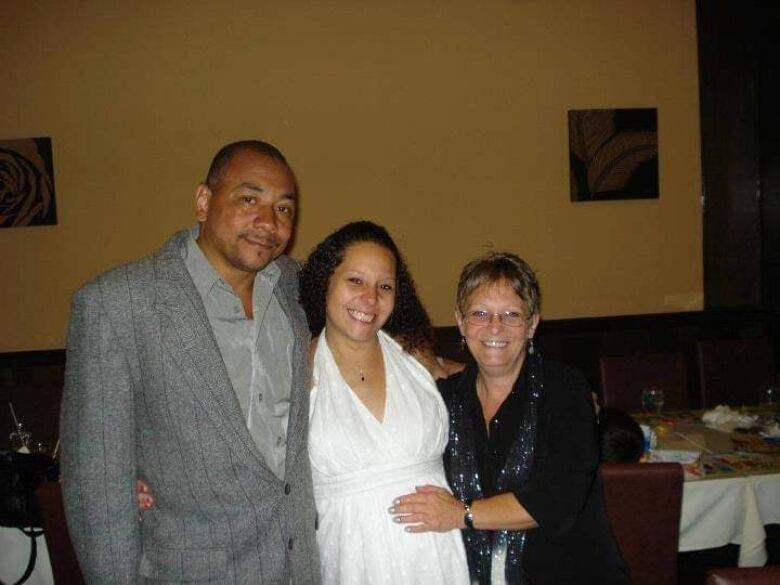 A woman in a white dress smiles between a man and a woman.