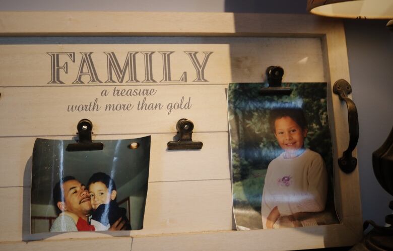 A wooden board with two photographs, one of a man holding a baby boy and another of a young girl.