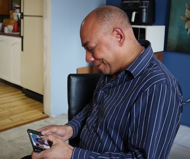 A man holding a phone smiles as he looks at the phone.