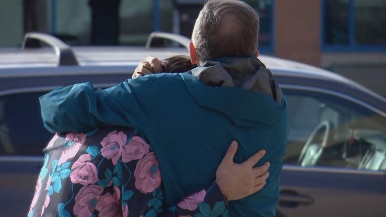 Two men, one in a floral blazer and another in a jacket, hug outdoors