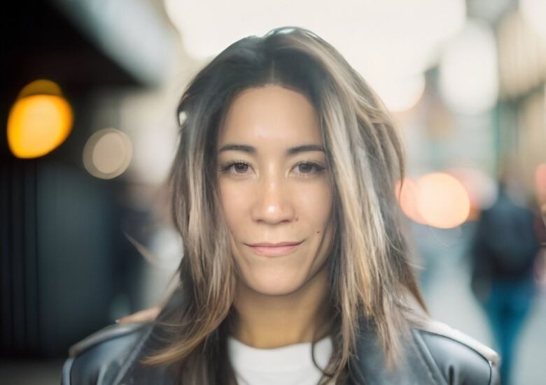 A woman in a leather jacket and white t-shirt looks into the camera.