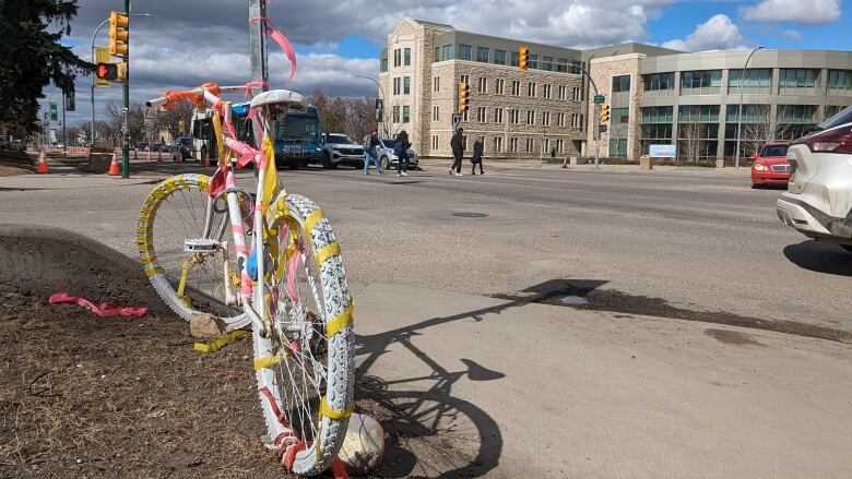 A white-painted bike wrapped with streamers and stuck to a pole on the corner of an intersection