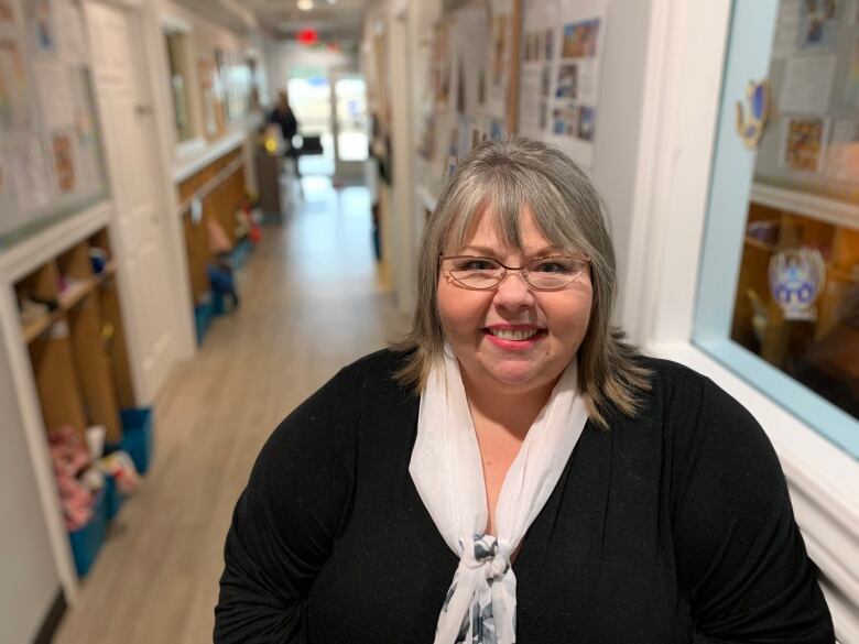 A woman with glasses stands in the hallway of a daycare.