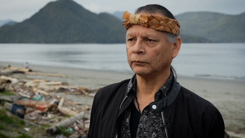 A man in a black sweater stands in front of beach. 