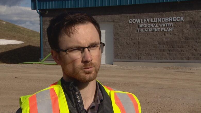 A man wearing a vest stands and looks at the camera.