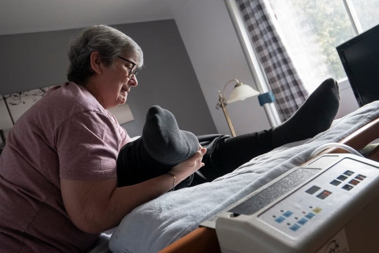 A woman adjust a man's legs on a mattress. 