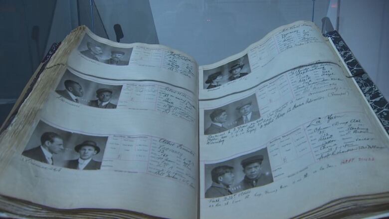 A historic book in a glass case. there are black and white mug shots and handwritten notes on the pages.