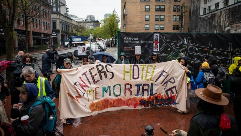 People gathered in a street holding a banner, which says Winter Hotel Fire Memorial