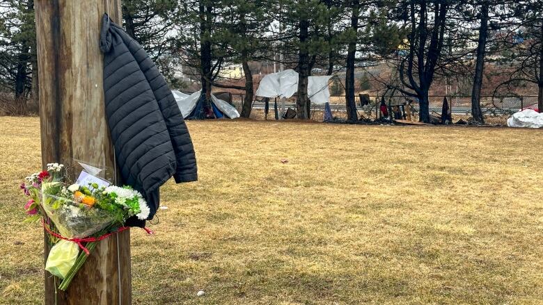 A flower bouquet on a telephone pole with a grassy field in the background with tents and debris in the background around several trees.