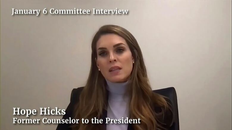 A woman wearing a blazer, a turtleneck and with brown hair several inches past her shoulder is shown in closeup in a still taken from a video recording.