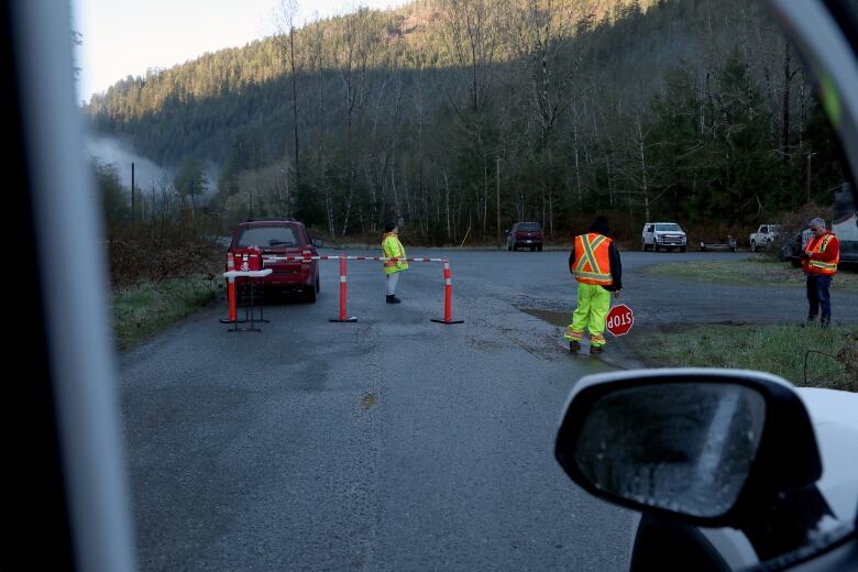 Pylons block access on a road to a lagoon. Three people is safety vests are standing nearby.