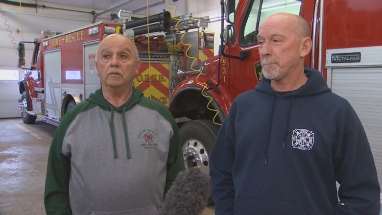 Two men stand in front of a fire truck