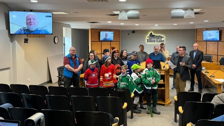 A group of children in hockey jerseys and some adults in a conference room. 