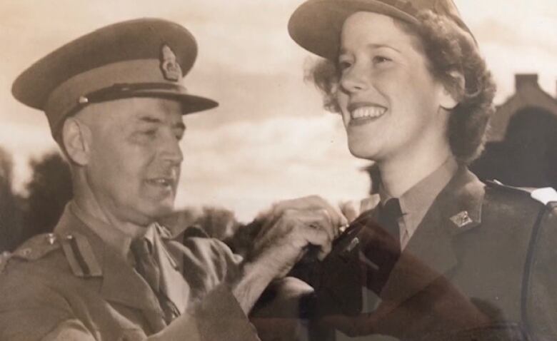 A sepia photo of a young woman in military uniform having a pin placed on her by an older man also in military clothing.