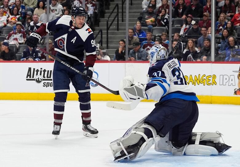 A goaltender stops a goal. Another hockey player stands in front of him.