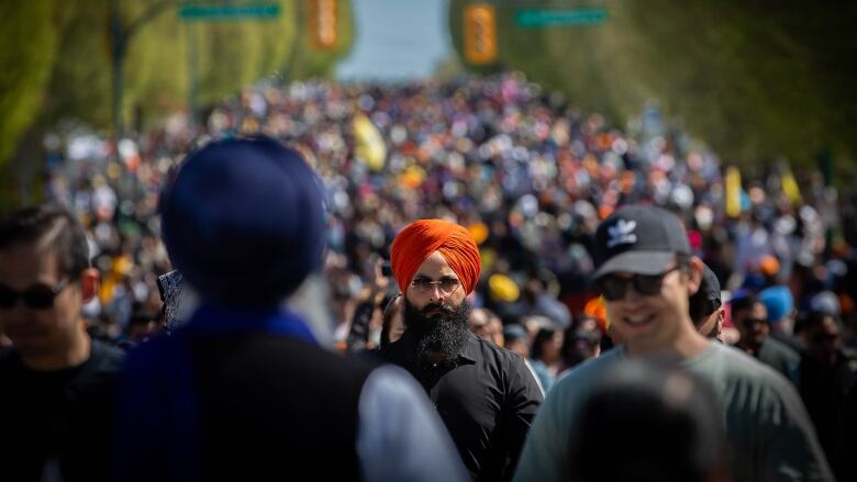 Thousands of people are seen marching down a street, with a turbaned man in focus at the centre of the shot.