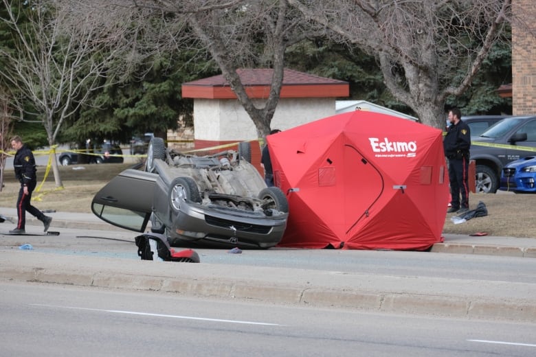 there is an upside down vehicle, car pieces scattered on the road, and police walking around