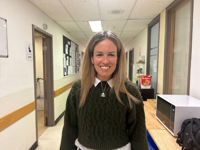 blonde woman in a green sweater with white collar standing in a hallway.