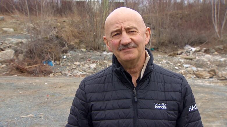 A man stands in a clearing and looks at the camera