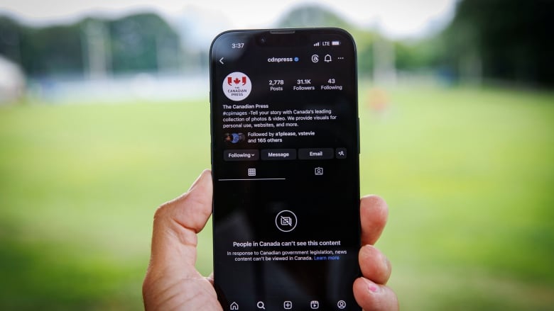 A hand holding a smartphone showing the Canadian Press Instagram page blocked.