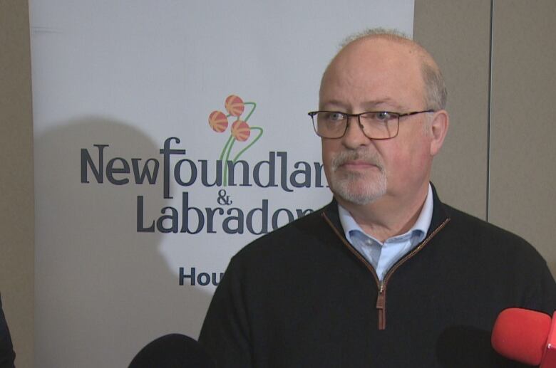 A man with glasses stands in front of a Newfoundland and Labrador government banner.