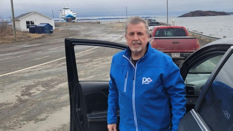 A man in a blue jacket standing outside a car.