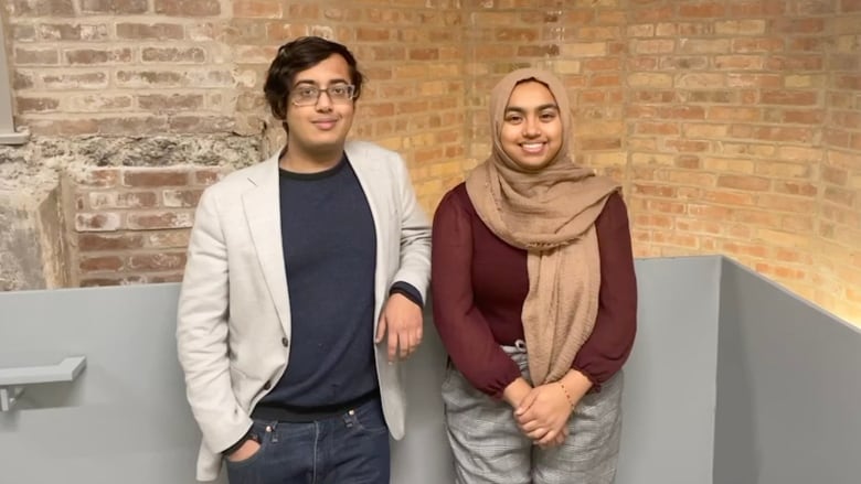 A young man and woman standing in front of a brick wall.