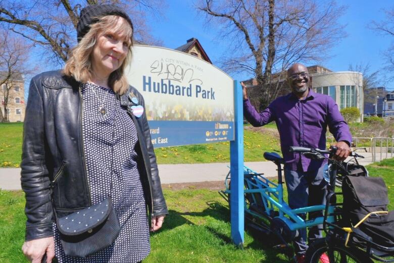 A woman stands at the left side of the frame and a man stands at the right, they are in front of a sign that says Hubbard Park.