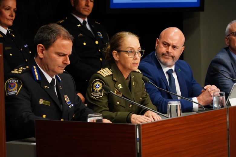 Police in formal attire speak at a microphone.